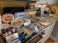 Wide view of trays and kitchen accessories arranged on stovetop and counter showing trays in glass, plastic, metal, and ceramic along with packaged utensils and skewers.