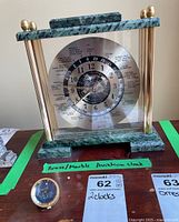 Front view showing the brass and green marble frame with world time zone markings and 24-hour dial.