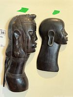 Two carved wooden African tribal busts mounted on wall, showing front and side profiles.