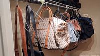 Various bags hanging on a rod including the Bentano patterned bag and multiple fabric and leather bags in brown, blue, and black tones