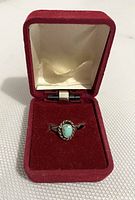 Small turquoise ring in an open red velvet ring box with a cream inner lining.
