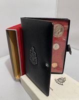 Genuine black leather case embossed with crest and containing clear view of several coins inside, set placed inside red velvet slip box with original certificate insert and shipping box.