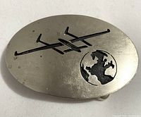 Front view of oval metal buckle with cut-out design of Voyager airplane and Earth.