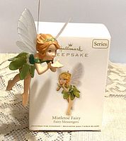 Front view of the Hallmark Keepsake Mistletoe Fairy hanging ornament next to its original box, showing detailed fairy figure with wings and green dress.