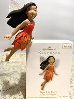 Side view of tiger lily fairy ornament suspended in front of original box showing design and size