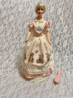 Full view of Barbie doll in costume with stand and brush on lace background
