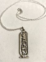 Front view of the necklace showing the detailed silver-tone Egyptian cartouche pendant with hieroglyphs.