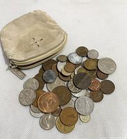 Photo showing variety of coins in different metals and designs spread next to a small beige leather zippered pouch