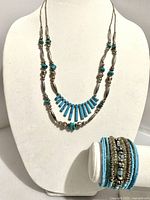 Southwest style necklace with turquoise-like beads and silvertone elongated beads displayed on mannequin with beaded bracelet beside.