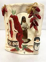 Full view of luminaria showing the textured pottery, red chili peppers, the figurine inside the cut-out, and artist signature.