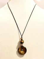 Necklace worn on white display bust showing carved tiger eye pendant and beads on black satin cord long necklace.