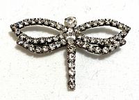 Front view of vintage dragonfly brooch with clear rhinestones set in silver-tone metal.