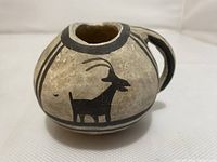 Close-up of small Southwest pottery pitcher showing black painted goat design and rounded bottom shape.