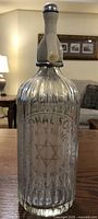 Front view of clear ribbed glass soda water bottle with embossed text and star emblem.