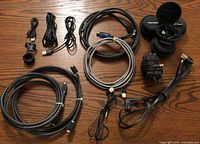 Photo showing a variety of electronic items including power adaptor, wireless earphones in black hard case, multiple HDMI and USB cables on a wooden surface.