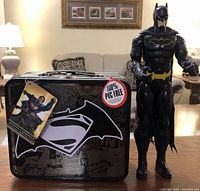 Photo showing the black metal lunchbox with Batman and Superman logos and a 12-inch Batman figurine standing beside it.
