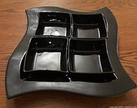 Black ceramic square platter with four nested square bowls inside, showing glossy finish and wavy edges of platter.