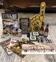 Full lot view showing grouped Boston Bruins collectibles including bobbleheads, figurines, beer bottles, magazines, books, cards, foam finger, and coasters.