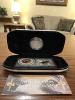 Opened black display case showing silver coin and Eddie Shore stamp with informational card