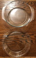Clear glass round casserole dish with handles and a clear glass pie dish on wooden surface.