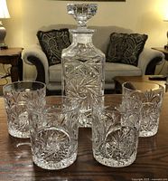 Crystal decanter and five matching glasses arranged on wooden table, showing intricate cut pattern.