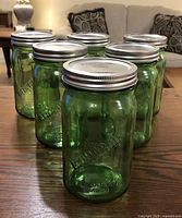 Front view of six green Bernardin Mason jars arranged on a table, showing embossed logos and metal lids.