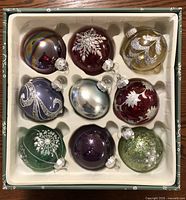 Box with nine hand decorated glass ornaments showing color and design variety in packaging
