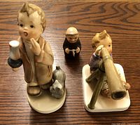 Three ceramic figurines as shown: boy with telescope, boy with candle and dog, small monk figure. The boy with telescope figurine is marked Occupied Japan.