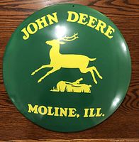 Full front view of the John Deere metal advertising button showing the logo and text on green background.