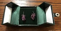 Pair of pink tourmaline dangle earrings displayed in green box on wood surface.