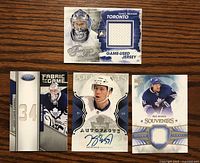 Four hockey cards displayed on wood surface: two James Reimer jersey cards, one Keith Aulie autographed card, and one Phil Kessel jersey card.