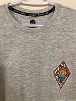 Close-up of front left chest showing the diamond-shaped colorful Maui & Sons logo patch and the fabric texture.