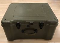 Closed view of green military barrack box showing the two black metal latches and handle on front side.