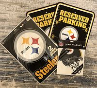 Photo displaying all items in the lot: two Reserved Parking signs, two large Steelers decals in plastic packaging, and one Steelers helmet magnet still packaged