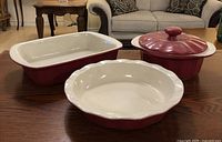 Three ceramic baking pieces: rectangular dish, round pie dish, and lidded casserole dish on a wooden table.