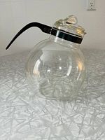 Full side view of the clear glass kettle with black handle on a countertop.