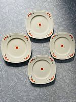 Four square ceramic cake plates shown from above, displaying the orange and black geometric Art Deco style pattern on a cream background.