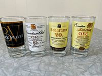 Front view showing all four glasses with distinct Canadian whisky labels: Black Velvet, Canadian Club, Seagram's V.O., and Canadian Schenley O.F.C.