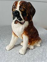 Front and left side view of the hand-painted Saint Bernard ceramic figurine showing the detailed facial features and glossy finish.