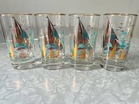 Photo of four cocktail glasses featuring turquoise and gold sailboat designs and gold rims.