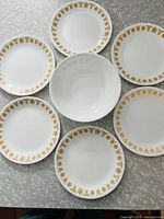Top-down photo of six plates arranged in a circular pattern around one bowl, all white with yellow-orange Butterfly Gold pattern on rims.
