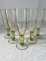 Photo of set of five lightly tinted green glass champagne flutes arranged upright on a grey surface, showing shape, color, and condition.