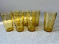 Set of seven golden amber Hazel Atlas Eldorado Gold Dot pattern drinking glasses arranged on a table, showing the faceted and raised dot surface texture.