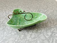 Top and angled side view showing green and white speckled ceramic surface and metal cigarette holder shaped with curls.