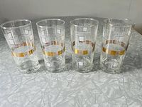 Four clear hi-ball glasses standing side by side showing geometric white designs and a middle gold band with gold rim accents.