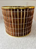 Side view of lampshade showing walnut strips on white woven framework with brass rims top and bottom.