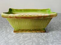Side view of rectangular ceramic planter with yellow-green bark textured design and footed base on gray surface.