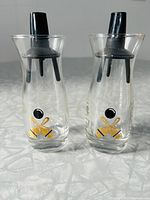 Two glass bottles with classic black and gold bowling graphics and black plastic pour spout stoppers placed side by side