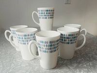 Front view of six Royal Tuscan Raindrop pattern cups showing their tall shape and horizontal raindrop design in blue, teal, and grey tones.
