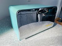 Front and side view of turquoise metal bread bin with chrome front and oval handle cutout showing overall look and condition.